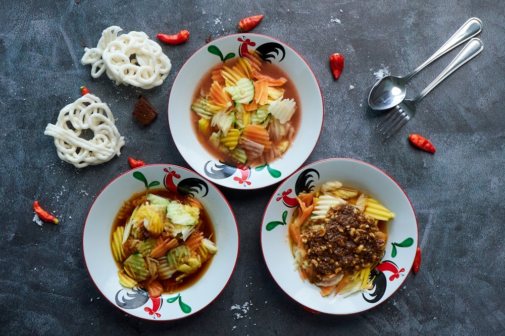 three bowls of food on a table with spoons