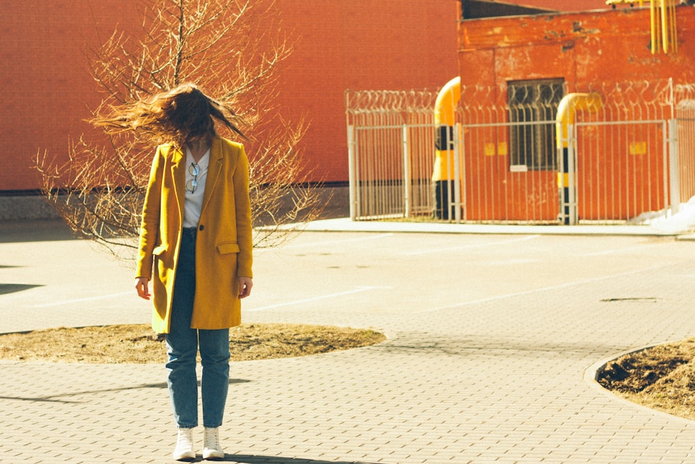 a woman in a yellow coat walking down a sidewalk