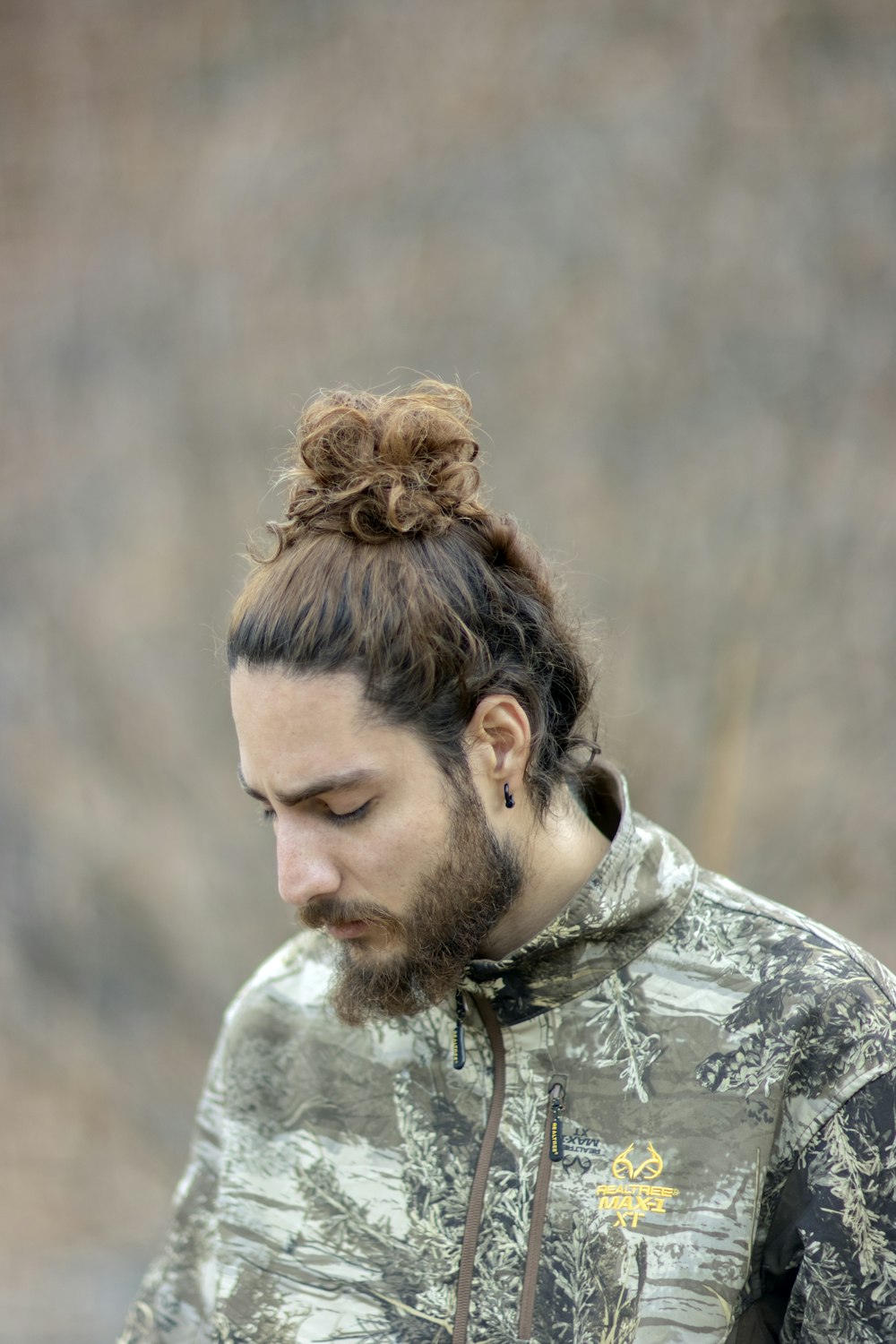 a man with a messy top knot looks down at his cell phone