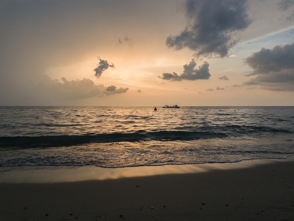 the sun is setting over the ocean with a boat in the distance