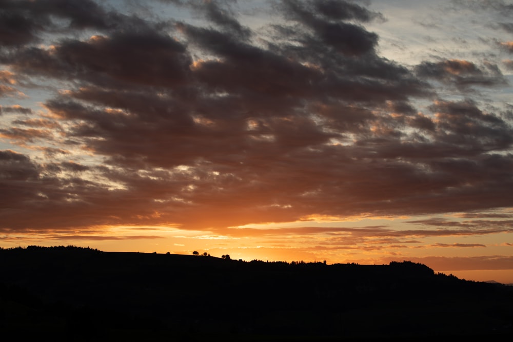 the sun is setting over a hill with trees