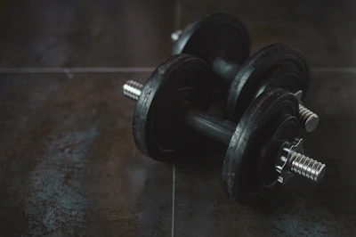 Close-up of matte black weightlifting gloves resting on a textured gym floor under moody lighting.