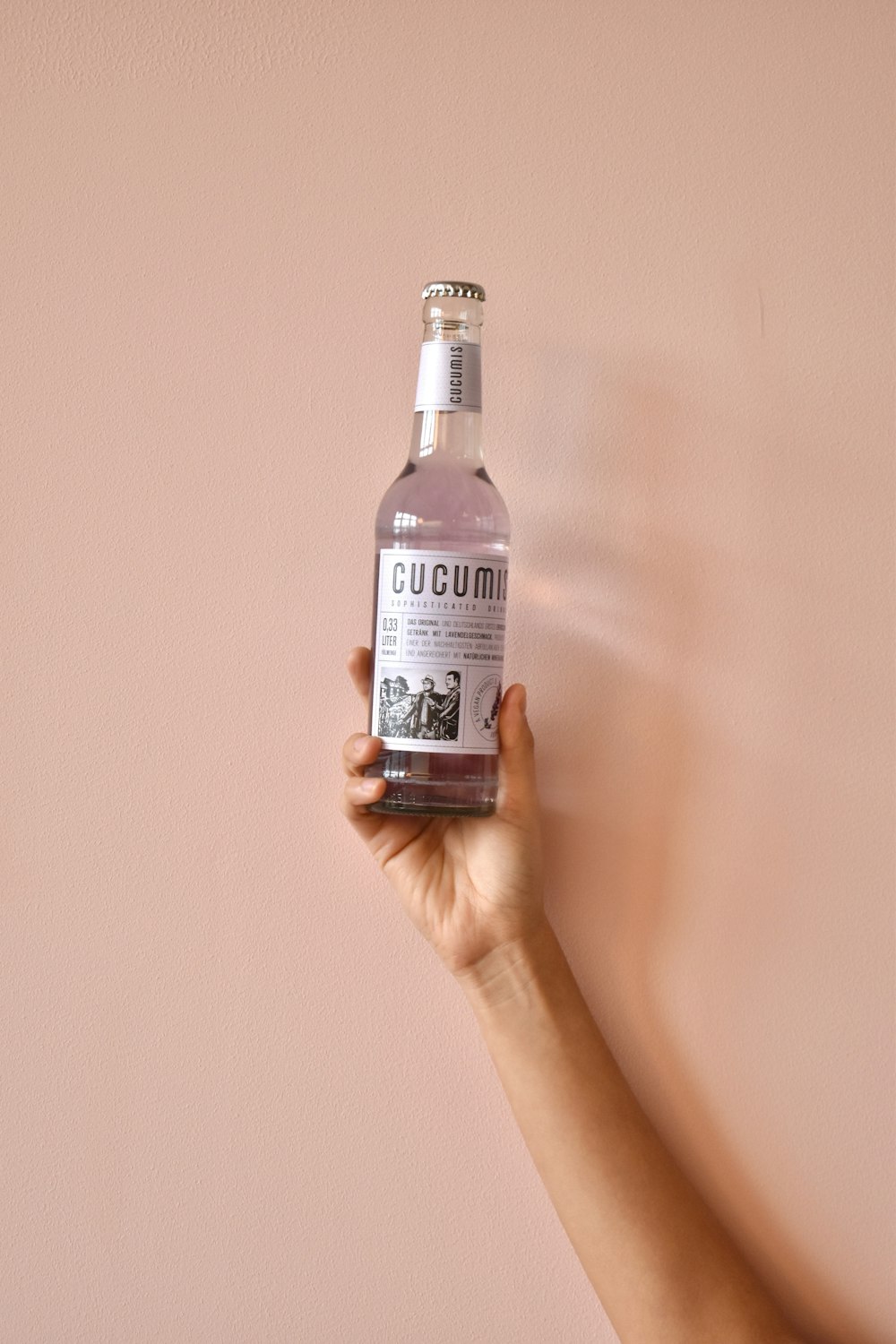 a hand holding a bottle of liquid against a pink wall