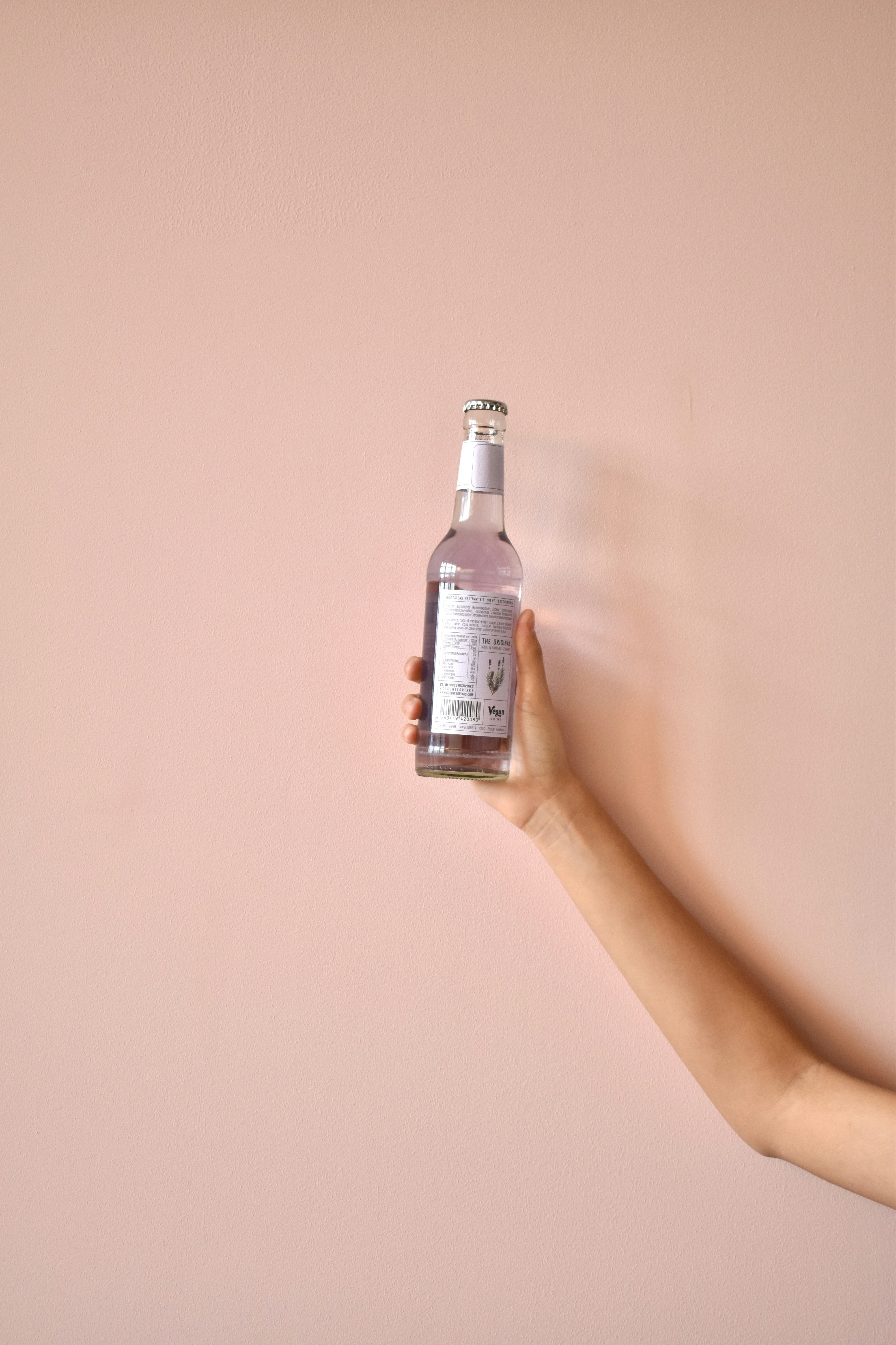 une main tenant une bouteille d’eau contre un mur rose