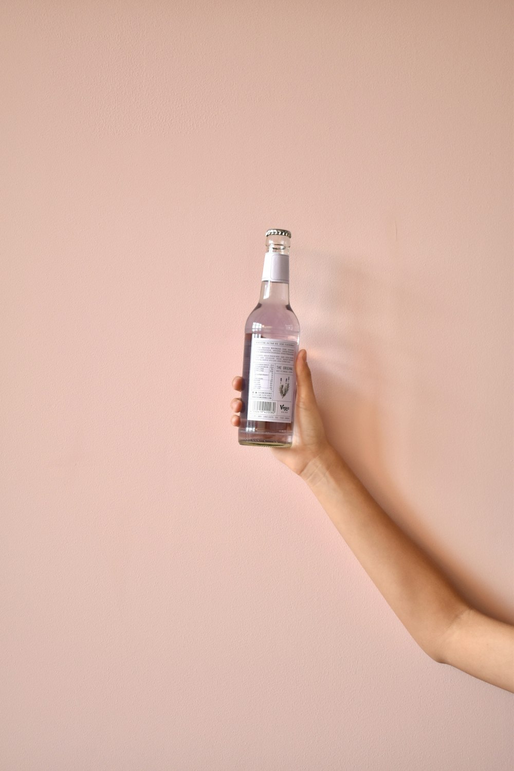 a hand holding a bottle of water against a pink wall