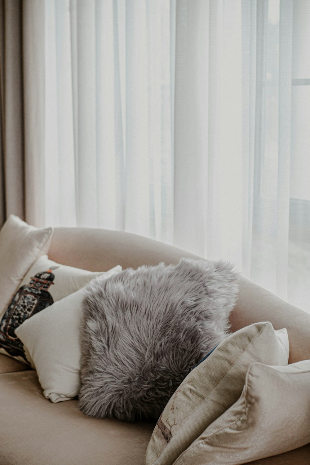 a round couch with pillows on it in front of a window