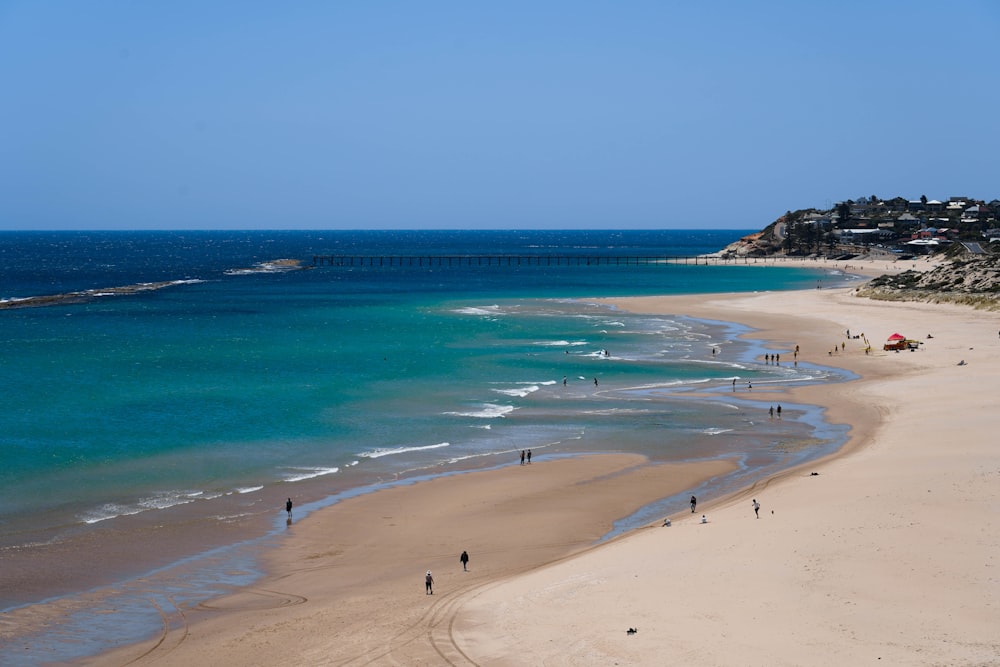 a beach with people walking on it and a bridge in the distance