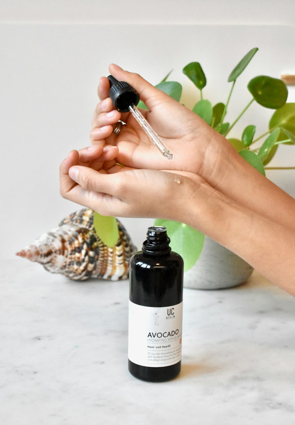 a hand holding a bottle of avocado oil next to a plant