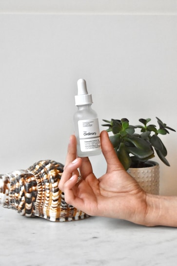 Close-up of a hand holding a bottle of soothing facial serum with fresh botanical ingredients in the background