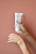 Close-up of a mother’s hands holding a Biomum stretch mark cream tube with soft peach background.