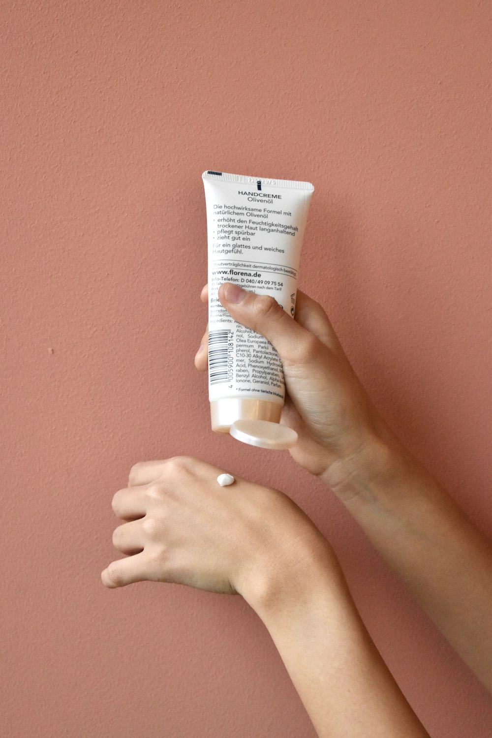 a hand holding a tube of sunscreen against a pink wall