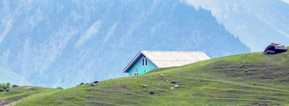 Ein kleines Haus auf einem grasbewachsenen Hügel mit Bergen im Hintergrund