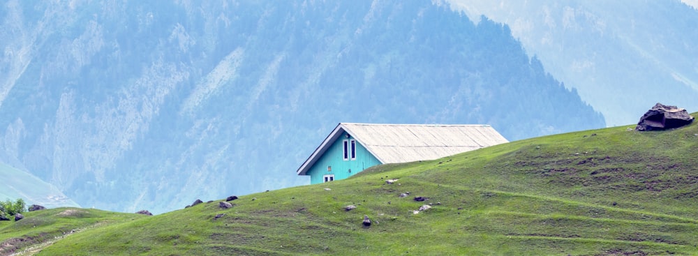 산을 배경으로 한 잔디 언덕 위의 작은 집