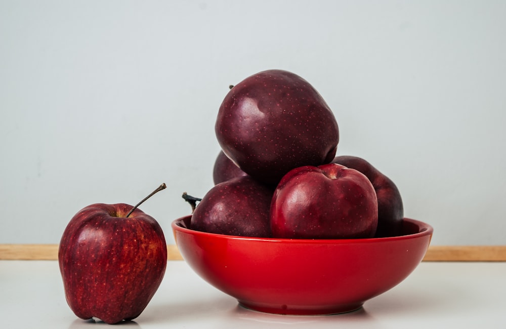 a red bowl filled with apples on top of a table