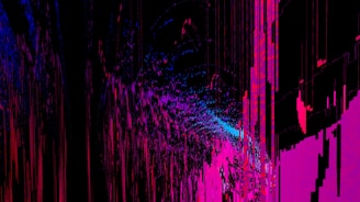 An abstract digital artwork featuring vibrant streaks and splashes of pink, blue, and purple against a predominantly black background. The pattern resembles a chaotic yet structured accumulation of vertical lines and scattered pixels, creating a vivid sense of movement and depth.