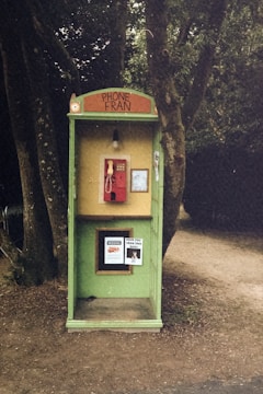 a green phone booth sitting next to a tree