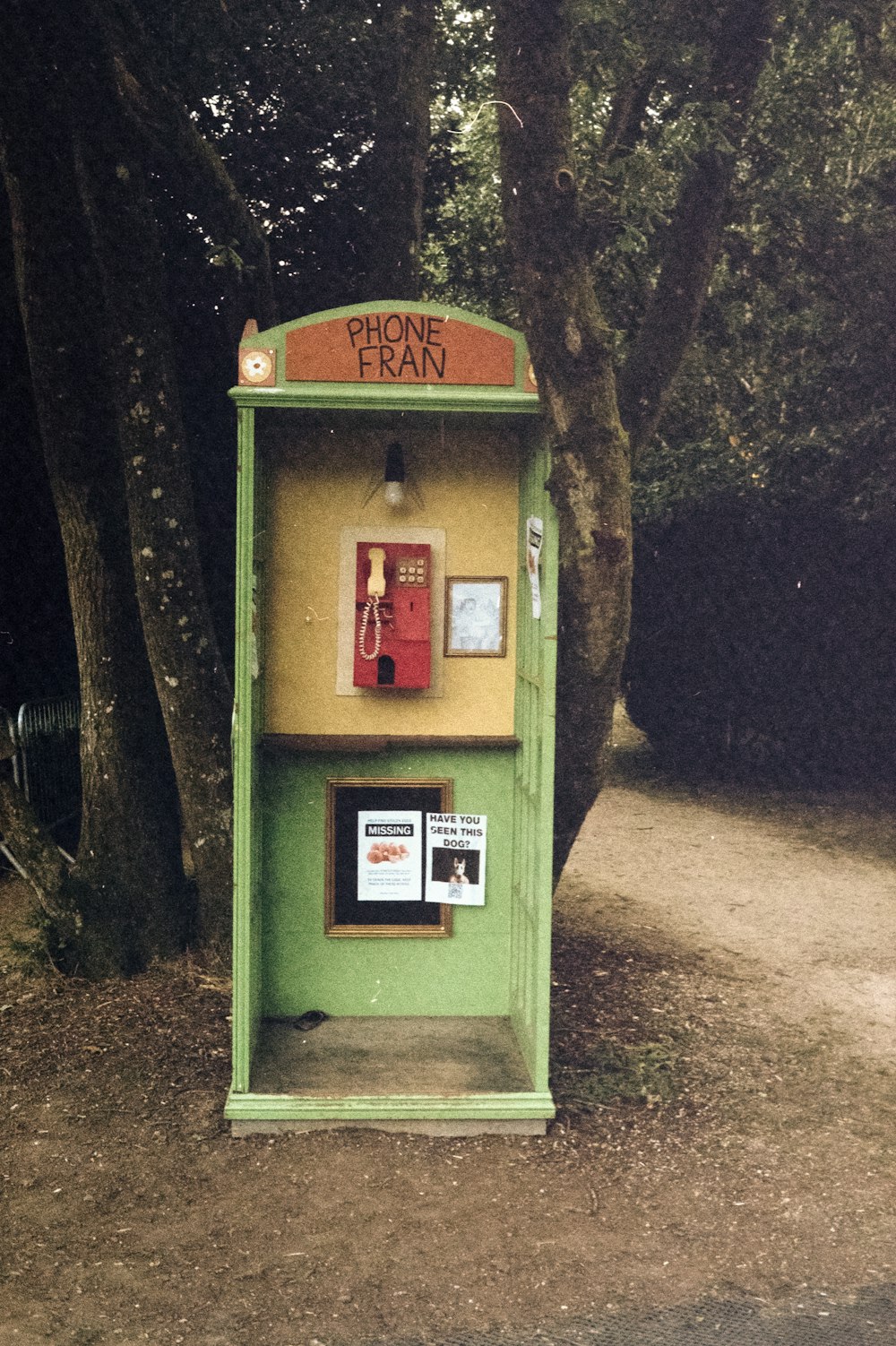 a green phone booth sitting next to a tree