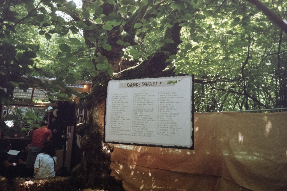 a group of people standing under a tree next to a sign