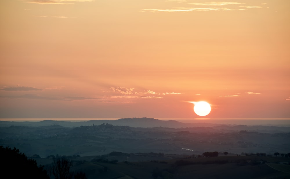 the sun is setting over the hills in the distance