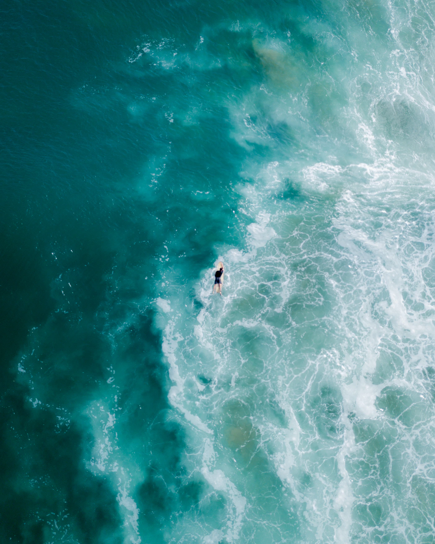Surfer riding a wave through deep teal ocean water