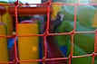 A red net is in the foreground, with a colorful inflatable play area visible behind it. The inflatable structure features bright green and yellow colors, hinting at a possible slide or obstacle course setup. Sunlight creates a lens flare, adding a warm glow to the scene.