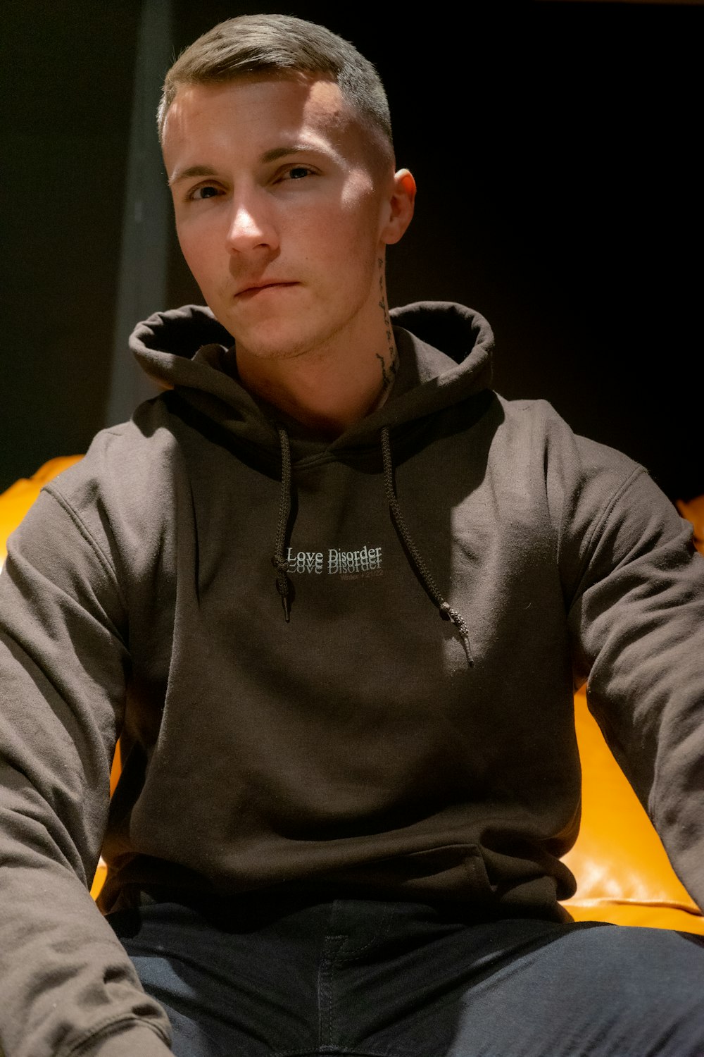 a young man sitting on a couch wearing a hoodie