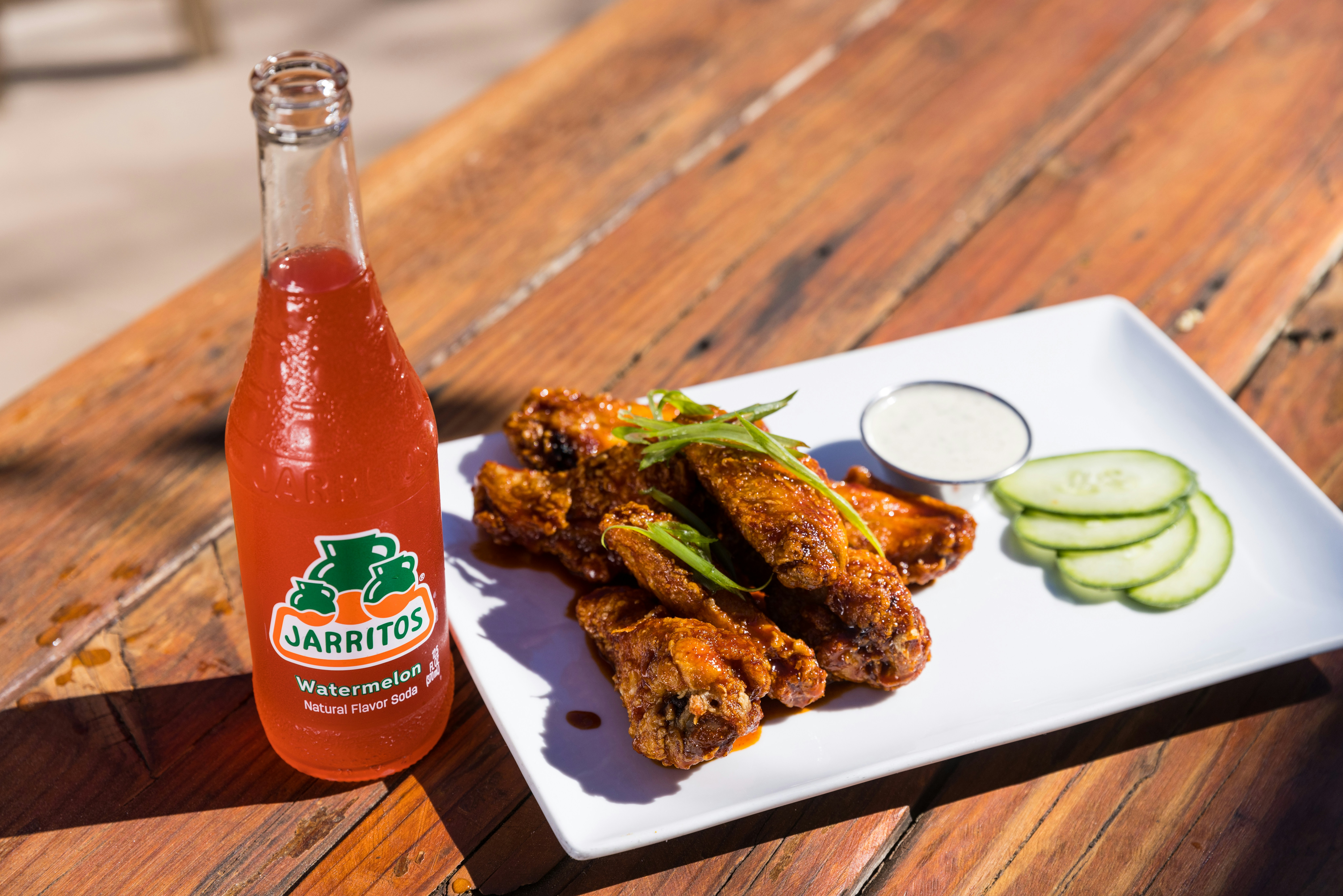 a white plate topped with chicken wings next to a bottle of soda
