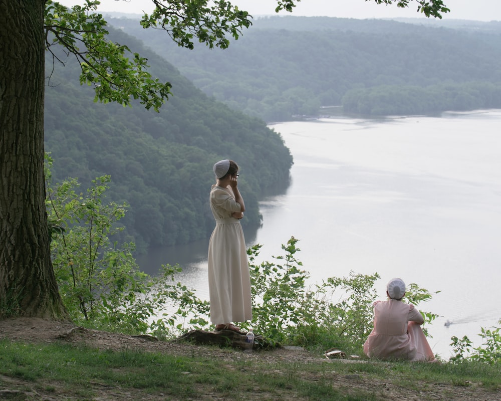 two women sitting on a hill overlooking a body of water