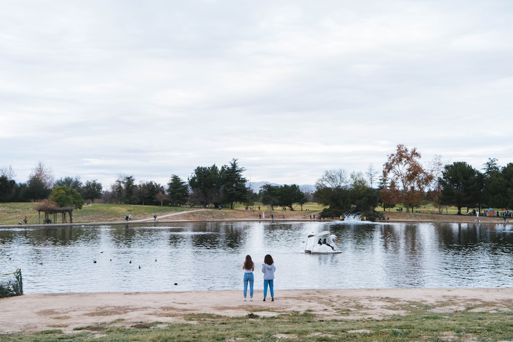 two people standing on the shore of a lake