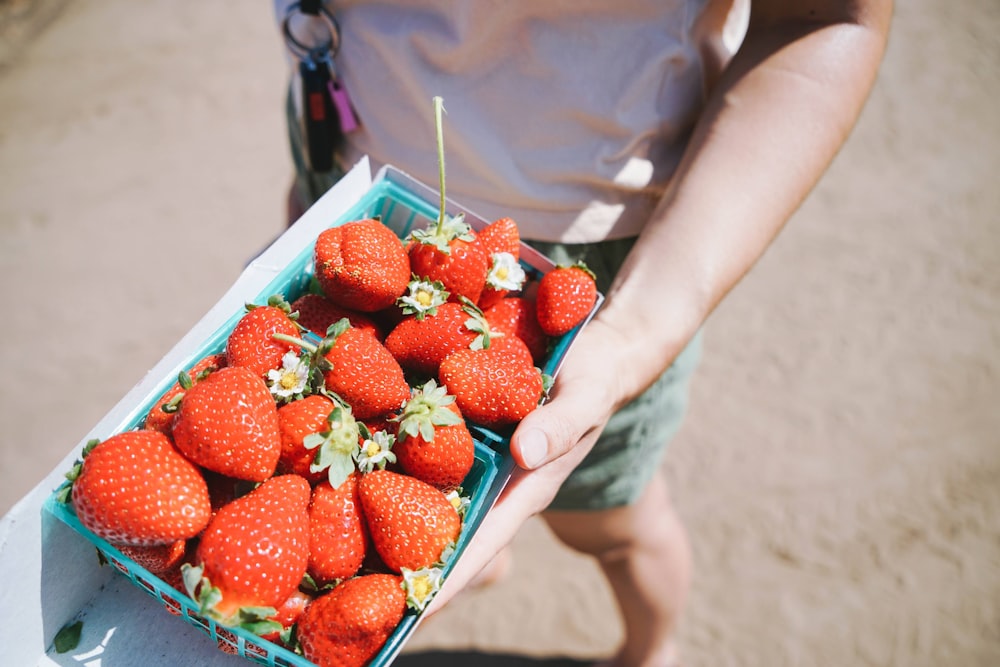 a person holding a box of strawberries on a beach