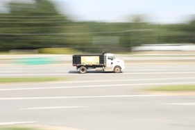a white truck driving down a street next to a forest