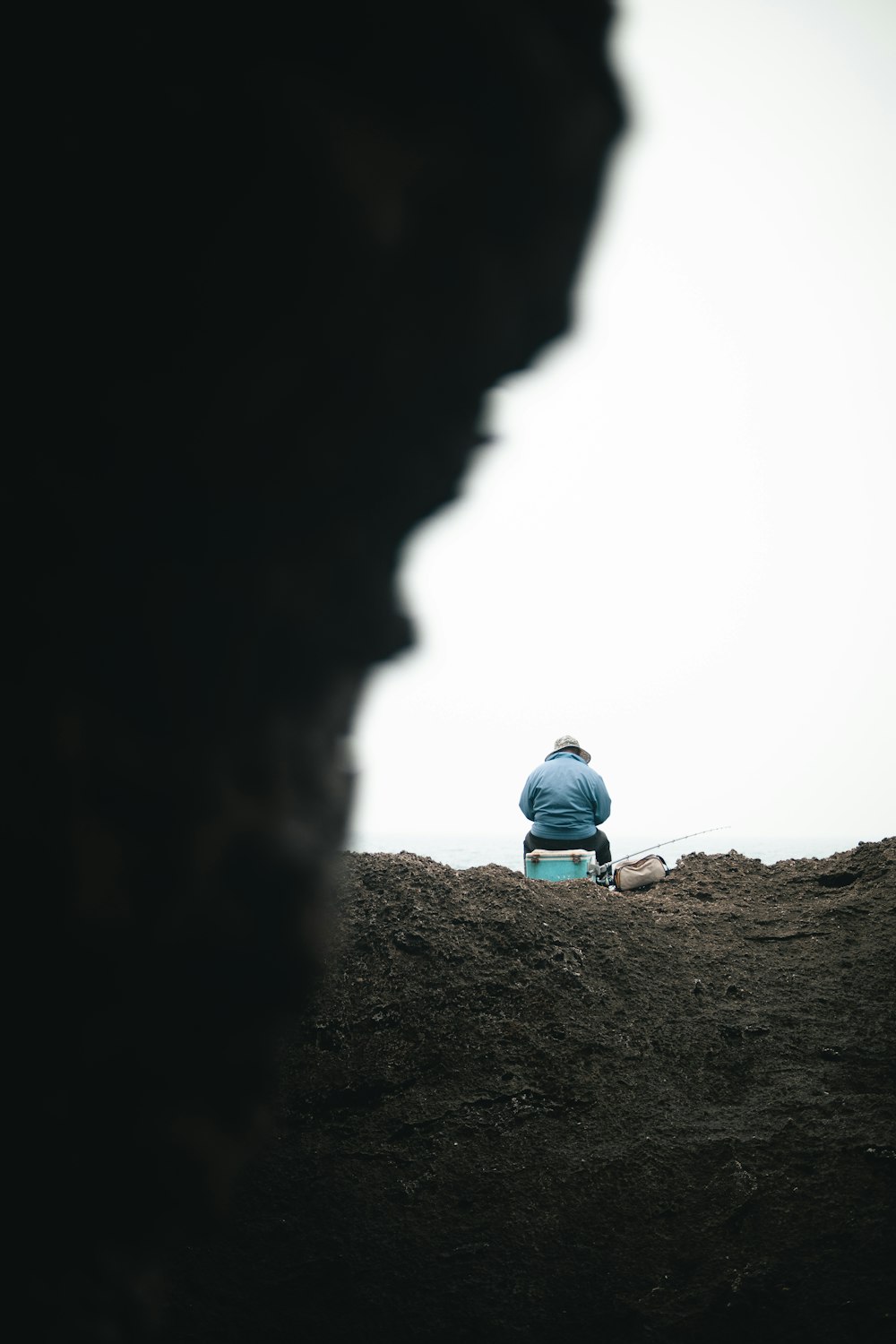 a man sitting on top of a hill next to the ocean