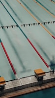 A swimming pool with several lanes marked by colorful lane dividers, including red and gold. Starting blocks are visible at the pool's edge.