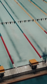 A swimming pool with several lanes marked by colorful lane dividers, including red and gold. Starting blocks are visible at the pool's edge.