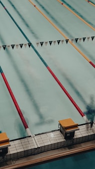 A swimming pool with several lanes marked by colorful lane dividers, including red and gold. Starting blocks are visible at the pool's edge.