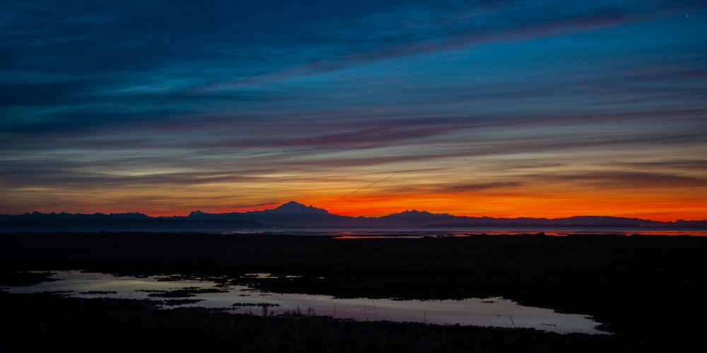 a sunset over a body of water with mountains in the background