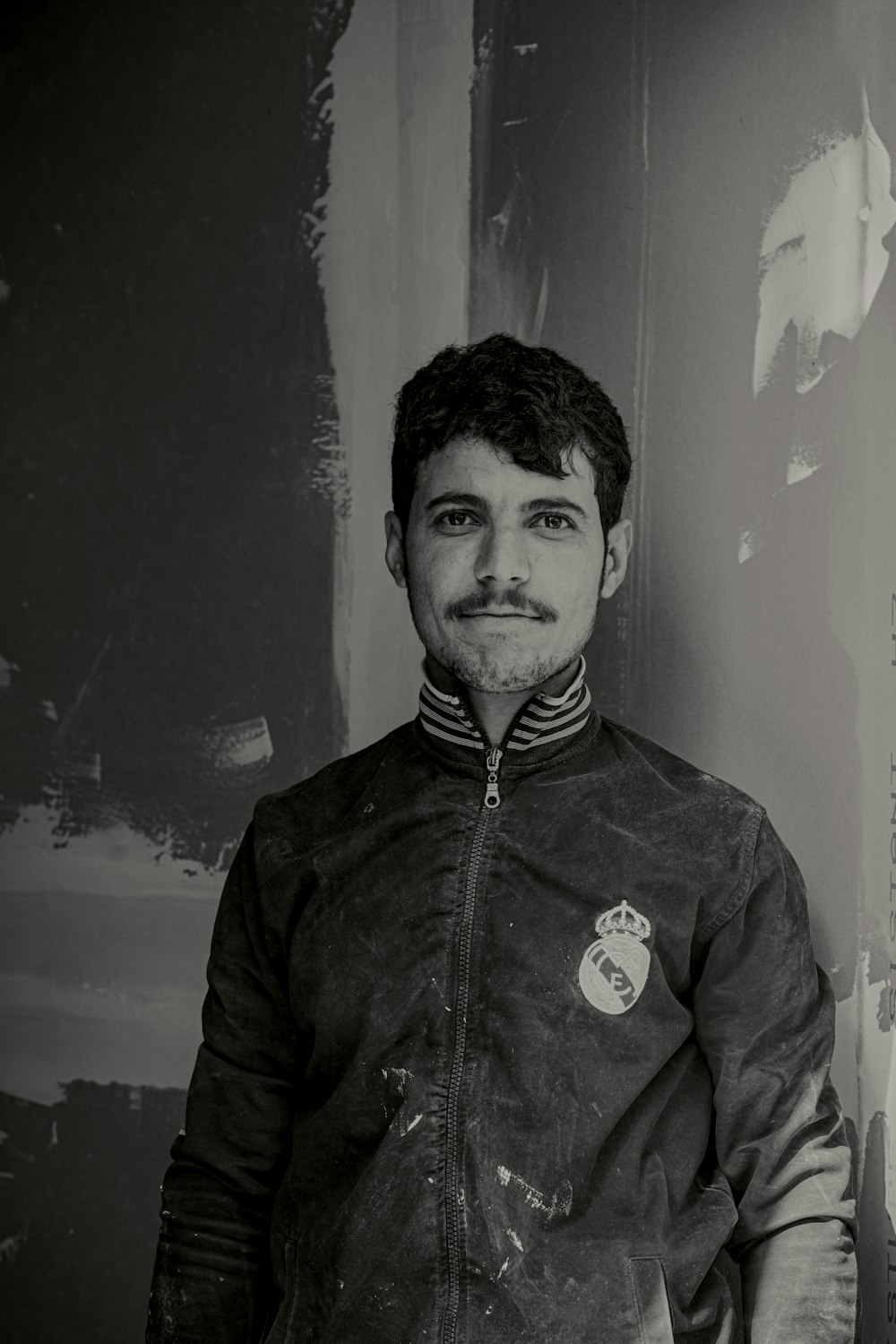 a man standing in front of a wall wearing a jacket