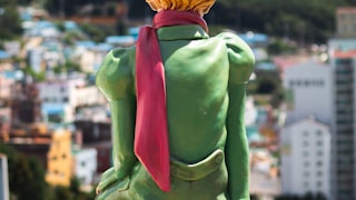 a statue of a woman sitting on top of a yellow fence by Youngeon Lee (@youngeonlee)