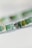A close-up view of a string of small, round beads in shades of green, with one silver bead featuring an engraved leaf pattern. The beads appear to be made of glass or a similar translucent material, creating a natural and artisanal look.