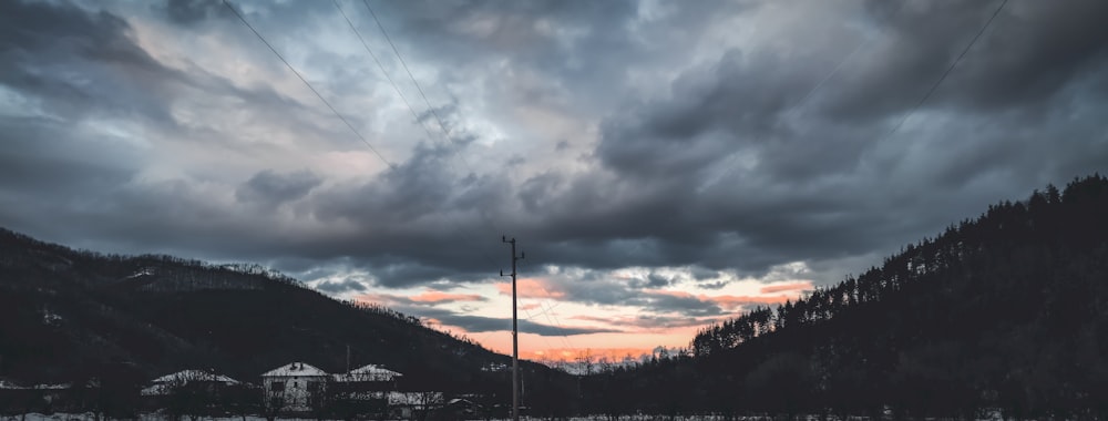 a cloudy sky over a mountain with a telephone pole in the foreground