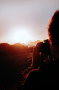 A documentary-style photo of a traveler capturing a sunset over rugged mountains, with a subtle map texture overlay.