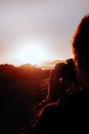 A golden hour shot of a lone traveler capturing the sunset over a rugged mountain landscape.
