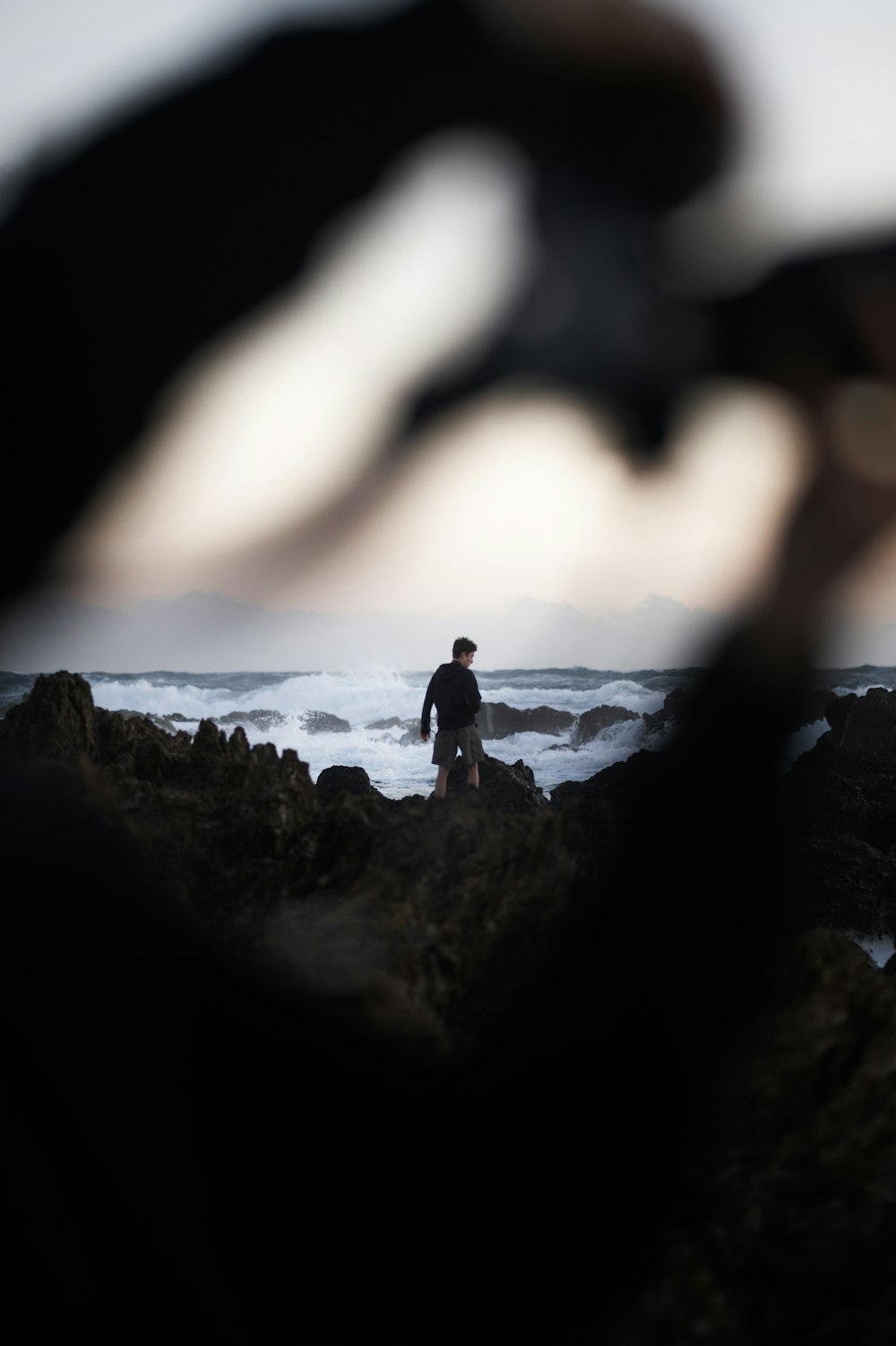 a man standing on top of a rocky beach next to the ocean