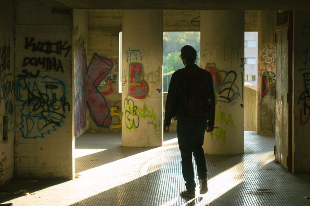 a man walking through a tunnel covered in graffiti