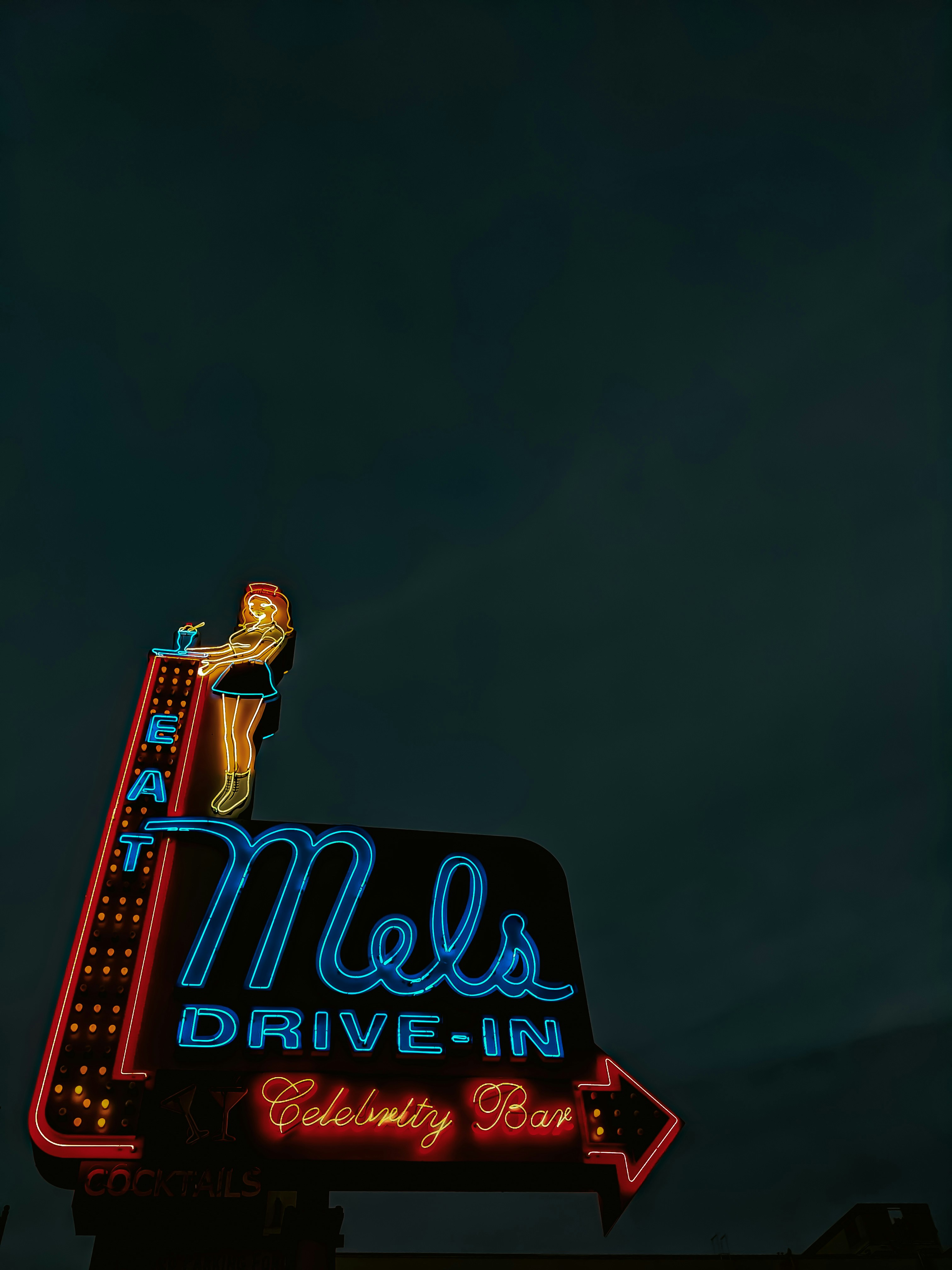 A neon sign that says mels drive - in in front of a building photo