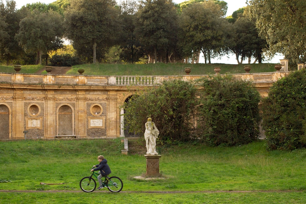 a man riding a bike past a statue in a park