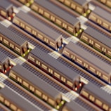Aerial view of a miniature model featuring multiple parallel train tracks with trains lined up on them. The scene includes intricate details such as train windows and track lines, suggesting a highly organized transportation system.