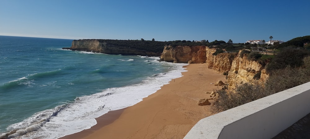 a sandy beach next to the ocean with a cliff in the background