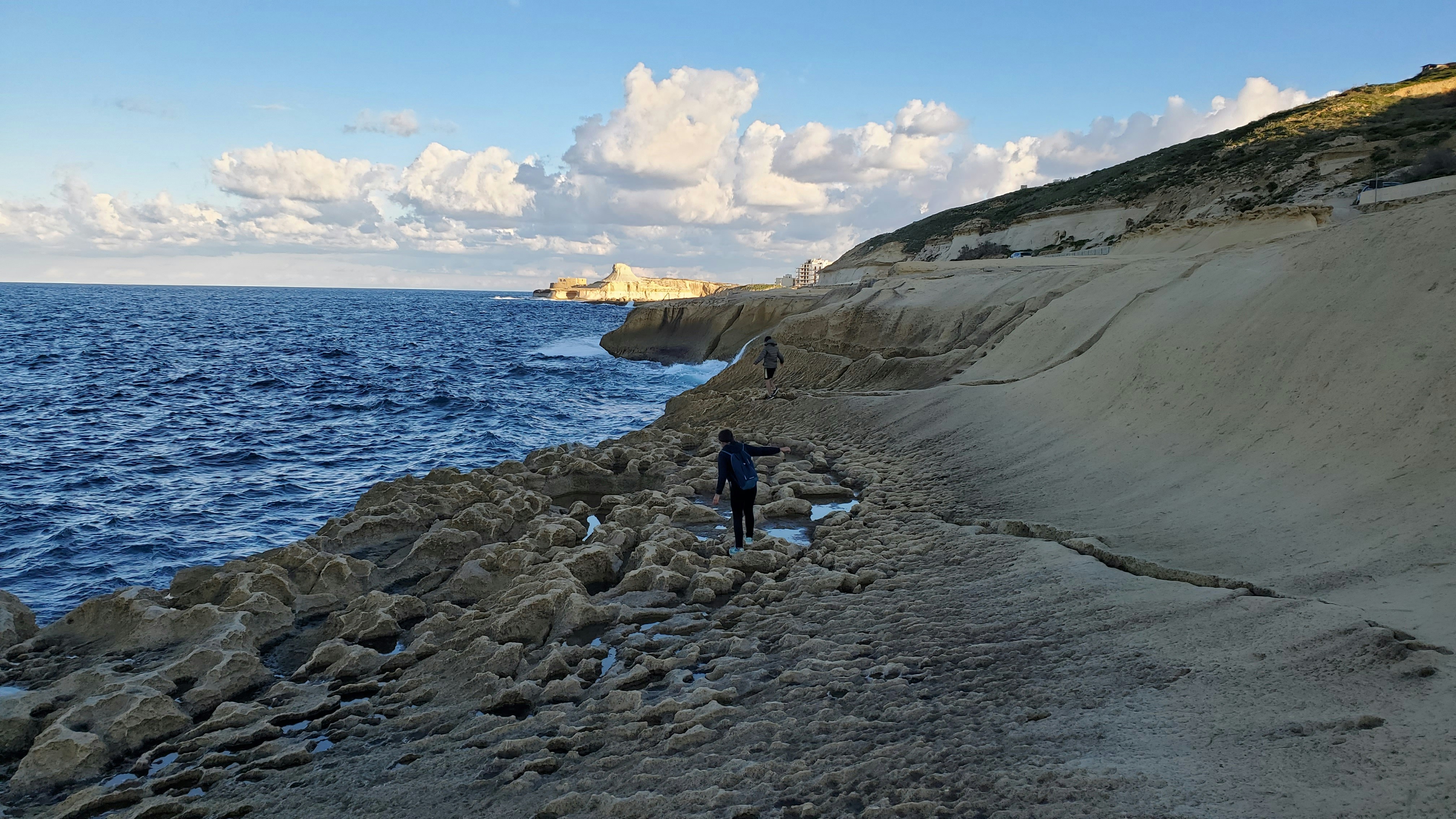 a person standing on a rocky beach next to the ocean, rocky shores of Gozo, Malta 