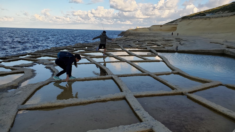 two people standing on a rocky beach next to the ocean